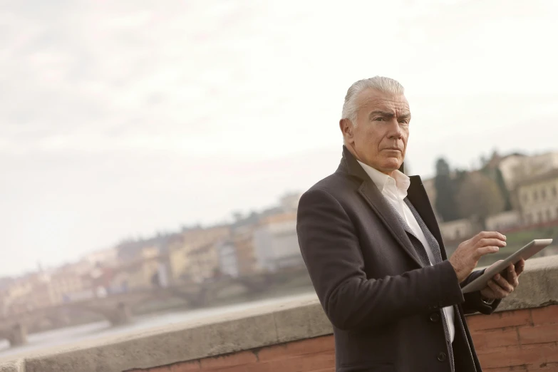 a man in a suit holding a tablet computer, an album cover, by Giuseppe Avanzi, on a bridge, giorgetto giugiaro, looking away from camera, till lindemann