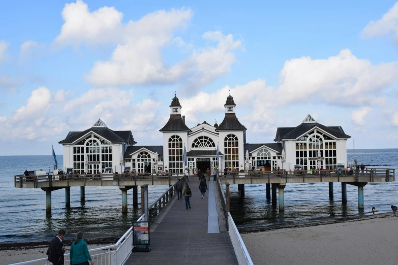 a pier with people walking on it next to the ocean, by Jan Tengnagel, pexels contest winner, art nouveau, white buildings, square, lower saxony, where a large
