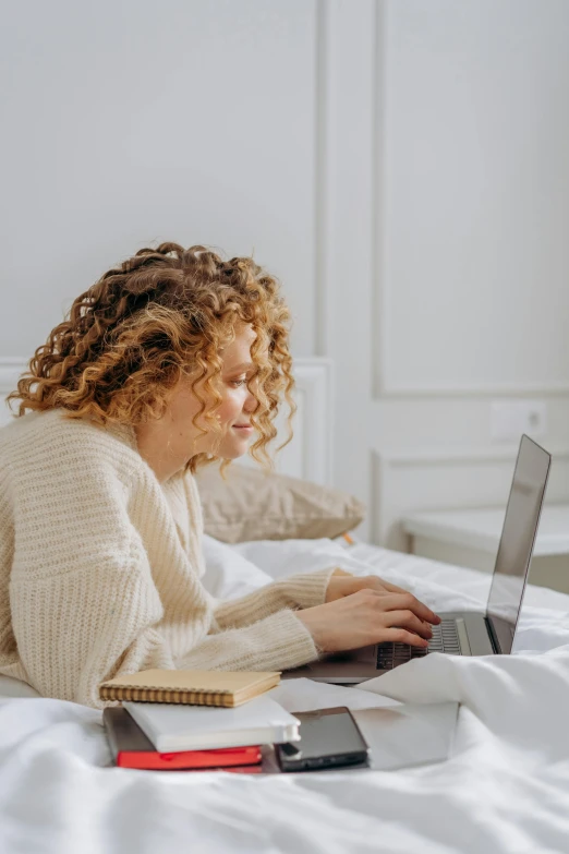 a woman laying on a bed using a laptop, trending on pexels, renaissance, curly dirty blonde hair, multiple stories, lightly dressed, curly brown hair