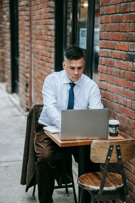 a man sitting at a table with a laptop, by Adam Rex, trending on pexels, street corner, wearing a shirt with a tie, thumbnail, greg rutkovsky