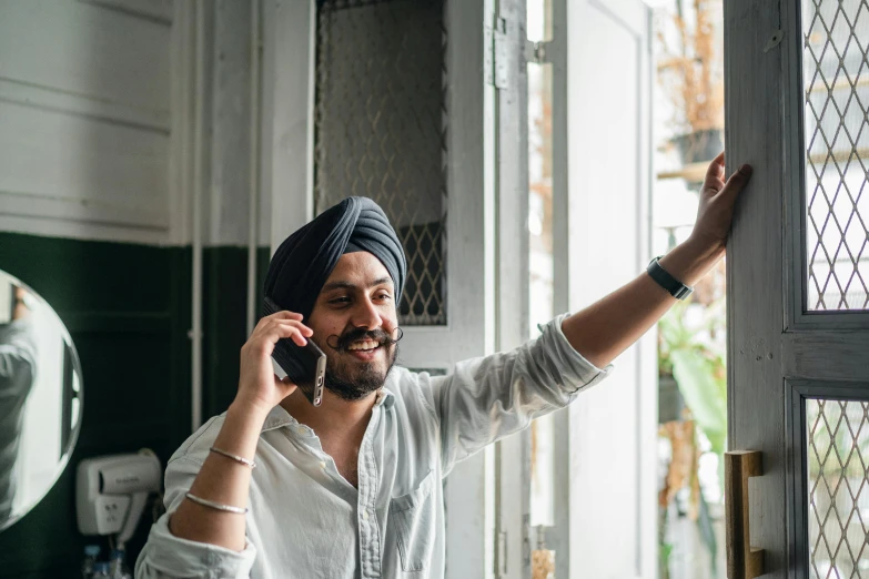 a man in a turban talking on a cell phone, inspired by Manjit Bawa, pexels contest winner, waving at the camera, looking out window, promo image, bringing people together