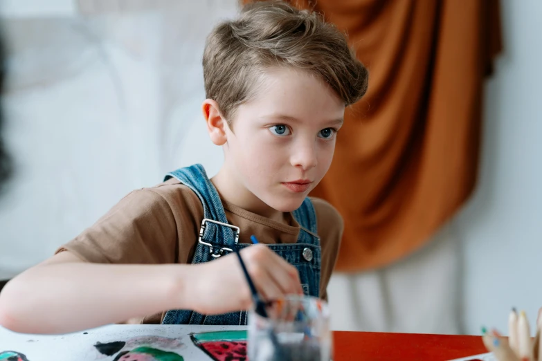 a little boy that is sitting at a table, inspired by Kyffin Williams, pexels contest winner, paint-on-glass painting, concentrated look, teenage boy, artist wearing overalls