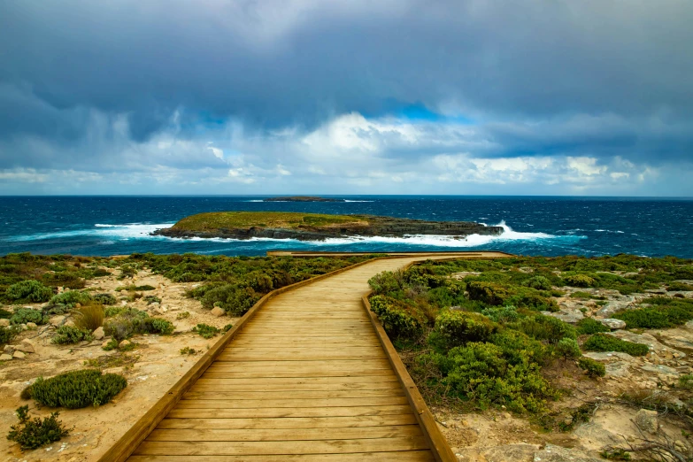 a wooden walkway next to the ocean on a cloudy day, pexels contest winner, australian outback, an island, stone paths, alvaro siza