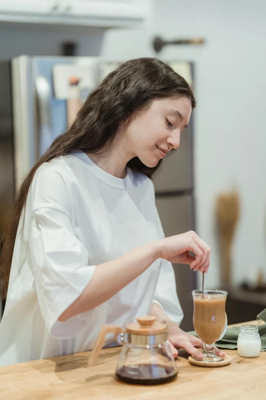 a woman sitting at a table with a cup of coffee, cooking, profile image, wearing a cute top, young woman with long dark hair