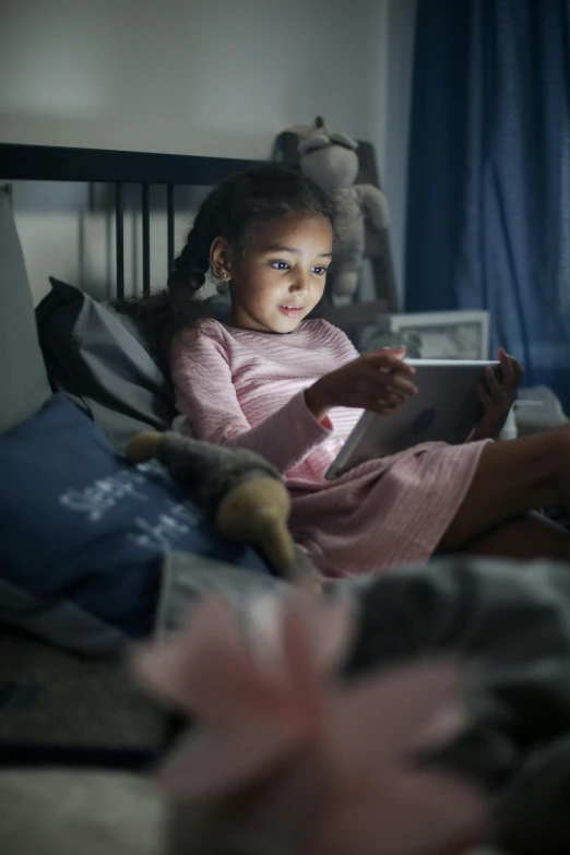 a little girl sitting on a bed reading a book, by Greg Rutkowski, high-tech devices, square, nigth, gettyimages