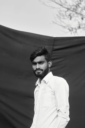 a man standing in front of a black backdrop, a black and white photo, by Max Dauthendey, samikshavad, around 20 yo, roadside, in front of white back drop, ((portrait))
