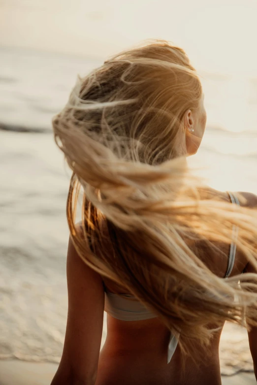 a woman sitting on top of a beach next to the ocean, pexels contest winner, renaissance, her hair blowing in the wind, close up of a blonde woman, back lit, spaghetti hair