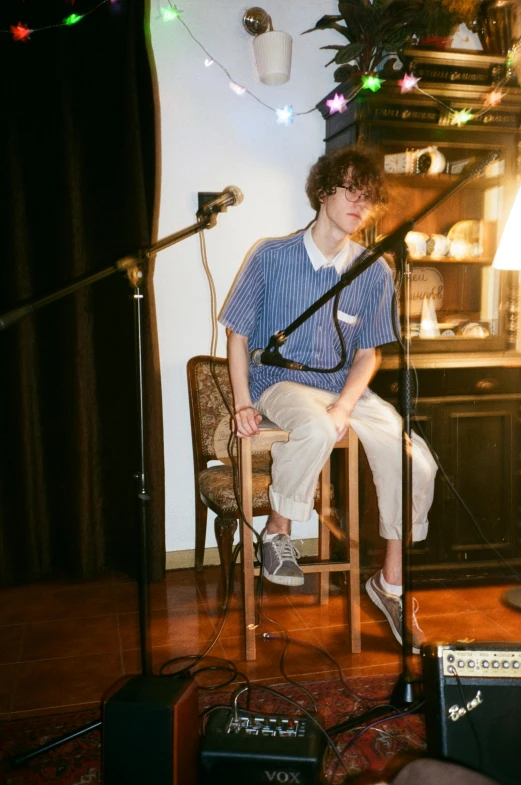 a man sitting on a chair in front of a microphone, an album cover, unsplash, finn wolfhard, studio kyoto, low quality photo, scanned