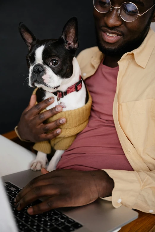 a man sitting in front of a laptop holding a small dog, trending on pexels, renaissance, ( ( dark skin ) ), wearing a cardigan, french bulldog, holding each other