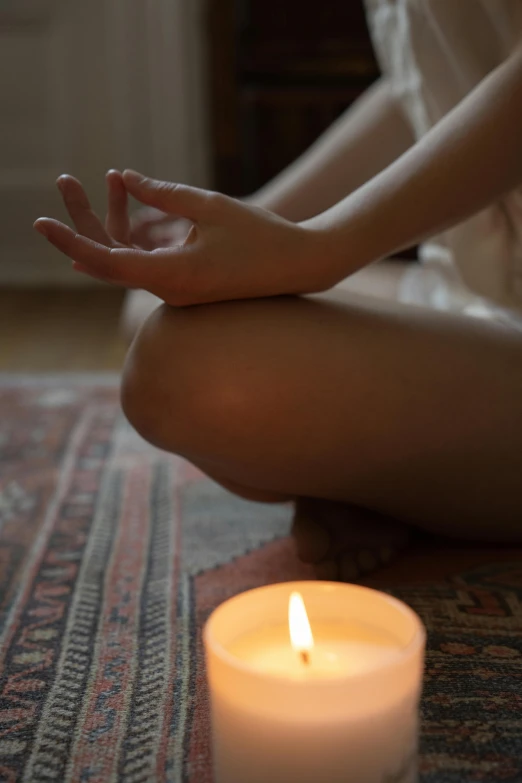 a woman sitting in front of a lit candle, anjali mudra, sydney hanson, sitting on the floor, atmospheric feeling