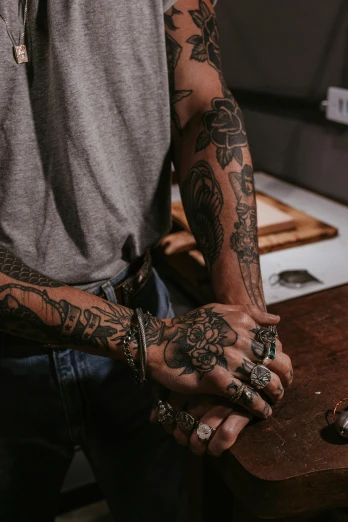 a man that has some tattoos on his arm, a tattoo, by Jessie Alexandra Dick, trending on pexels, process art, hand on table, intricate jewelry, sailor jerry tattoo flash, two arms
