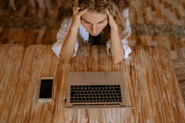 a woman sitting at a table with her head in her hands, trending on pexels, laptop, avatar image, broken down, wavy hair spread out