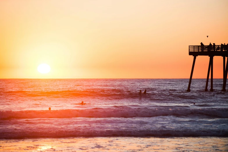 a group of people riding surfboards on top of a wave, pexels contest winner, romanticism, orange sun set, bold lighthouse in horizon, santa monica beach, a wooden