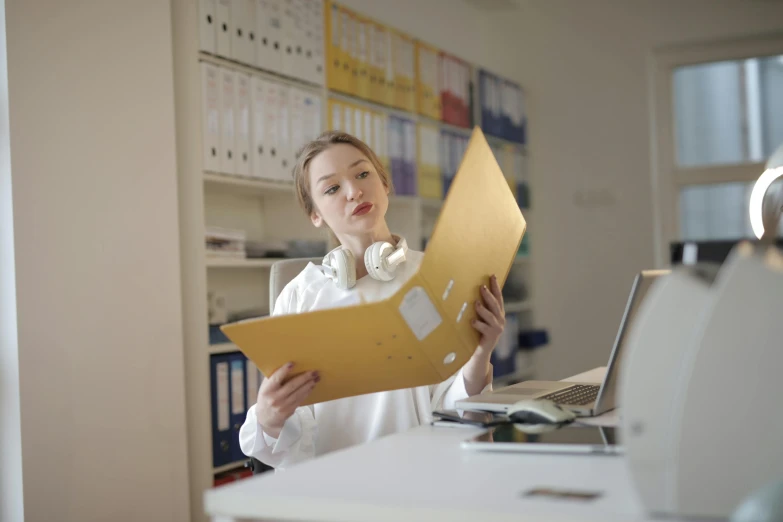 a woman sitting at a desk holding a folder, an album cover, pexels, in an call centre office, gold, wearing a labcoat, thumbnail