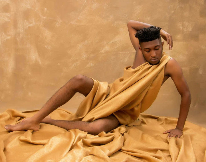 a man sitting on top of a bed covered in a yellow sheet, inspired by Thomas Blackshear, trending on pexels, renaissance, brown skin like soil, at a fashion shoot, tendu pose, gold silk