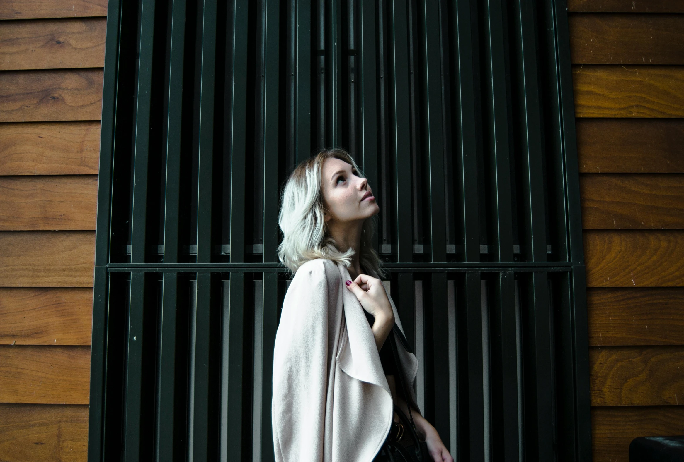 a woman standing in front of a metal gate, inspired by Elsa Bleda, unsplash, girl silver hair, woman is in a trenchcoat, beauty blade runner woman, young woman looking up