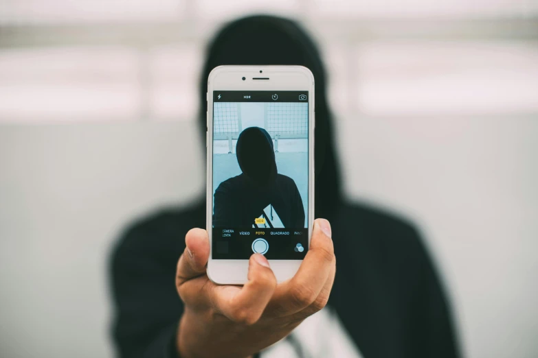 a close up of a person holding a cell phone, a picture, by Niko Henrichon, trending on unsplash, symmetrical cloaked figure face, an intruder, instagram selfie, ( ( dark skin ) )