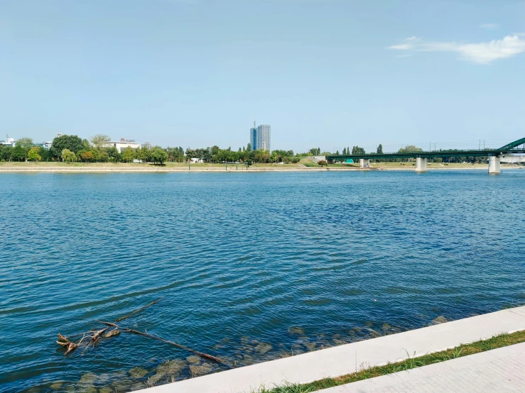 a large body of water with a bridge in the background, by Emma Andijewska, hurufiyya, vienna city, 1 0 0 meter in the distance, lake blue, gofl course and swimming