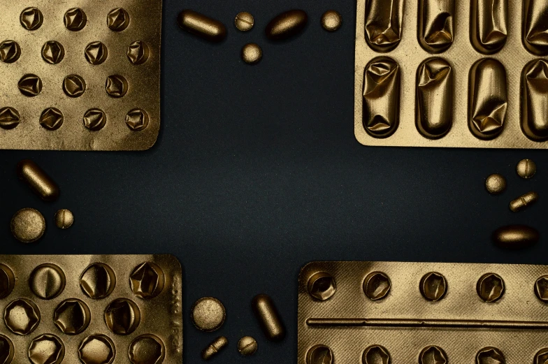 a group of chocolate molds sitting on top of a table, an album cover, deviantart, pills and medicine, carbon black and antique gold, thumbnail, digitally enhanced
