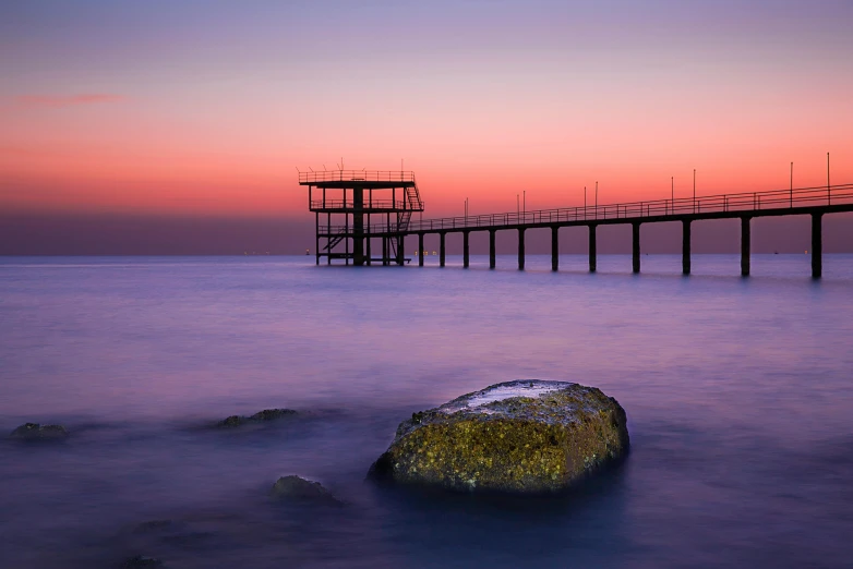 a large rock sitting in the middle of a body of water, by Konrad Witz, unsplash contest winner, romanticism, near a jetty, bridges, black sea, at gentle dawn pink light