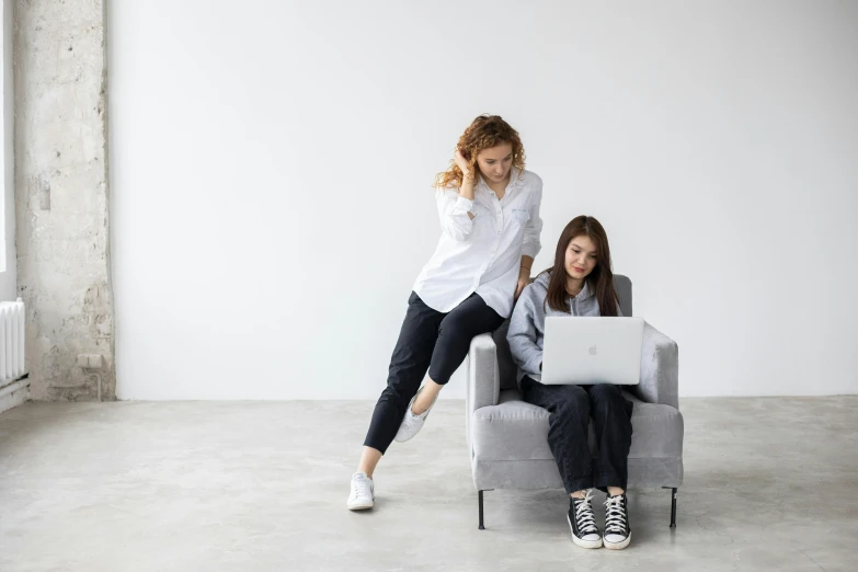 two women sitting on a chair with a laptop, trending on pexels, white, casual clothing, grey, in an action pose