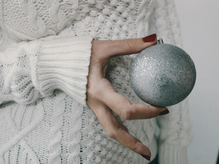 a woman in a white sweater holding a silver ornament, trending on pexels, grey, ball, gif, background image