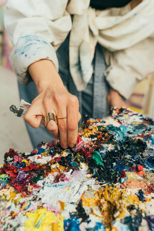 a close up of a person holding a paintbrush, a detailed painting, inspired by Shōzō Shimamoto, trending on unsplash, process art, artist wearing torn overalls, colorful torn fabric, rich palette, alyssa monks