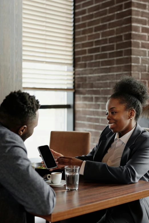 a man and woman sitting at a table looking at a tablet, by Carey Morris, pexels contest winner, woman in black business suit, afro tech, sitting on a mocha-colored table, flirting