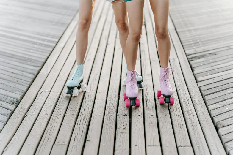 a couple of women standing next to each other on skateboards, a colorized photo, trending on pexels, detailed legs, mauve and cyan, a wooden, boardwalk