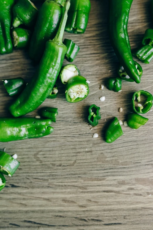 a pile of green peppers sitting on top of a wooden table, by Julia Pishtar, confetti, cut, multiple stories, pickle