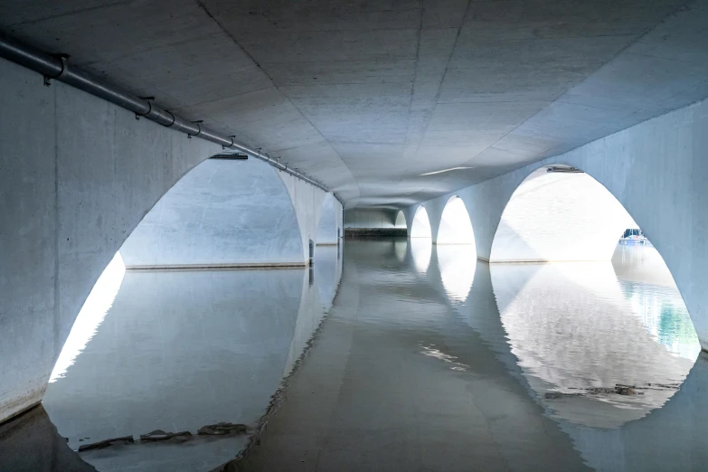 a man riding a skateboard up the side of a ramp, inspired by Tadao Ando, unsplash contest winner, minimalism, crawling in a wet sewer pipe, water mirrored water, symmetric lights, white stone arches