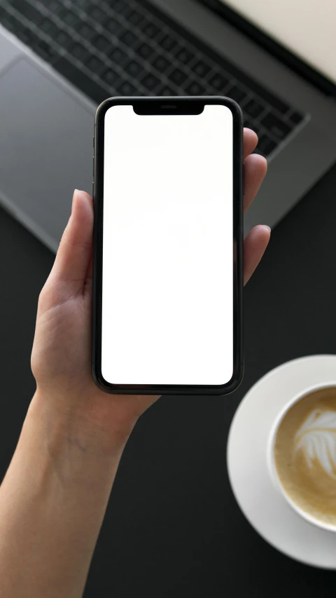 a person holding a cell phone in front of a laptop, with a white mug, shot on iphone 1 3 pro max, low quality photo, .ai