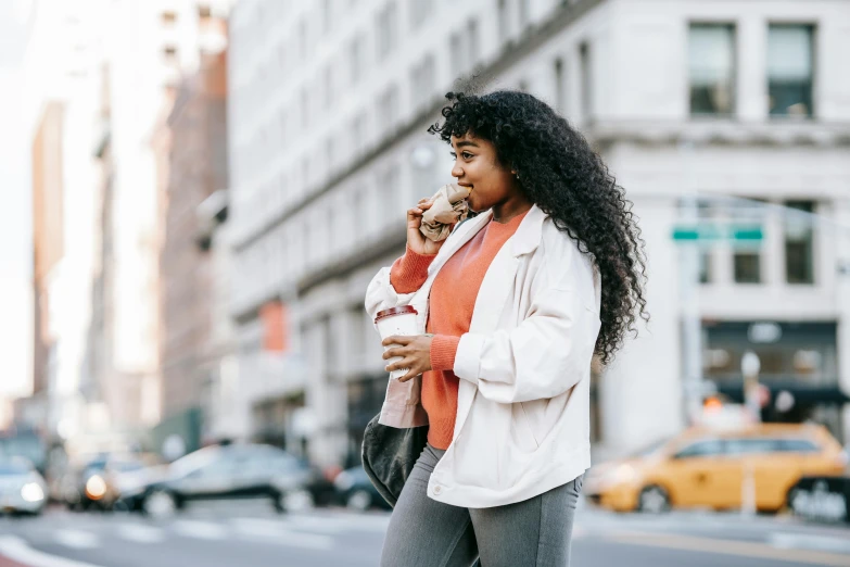 a woman walking down the street talking on a cell phone, by Carey Morris, trending on pexels, happening, eating a donut, long wild black curly hair, iced latte, plus-sized