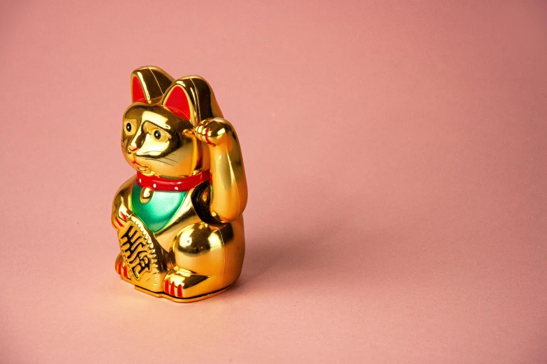 a gold figurine of a cat on a pink surface, a statue, trending on unsplash, cloisonnism, happy meal toy, asian man, chinchilla animal, gold and green