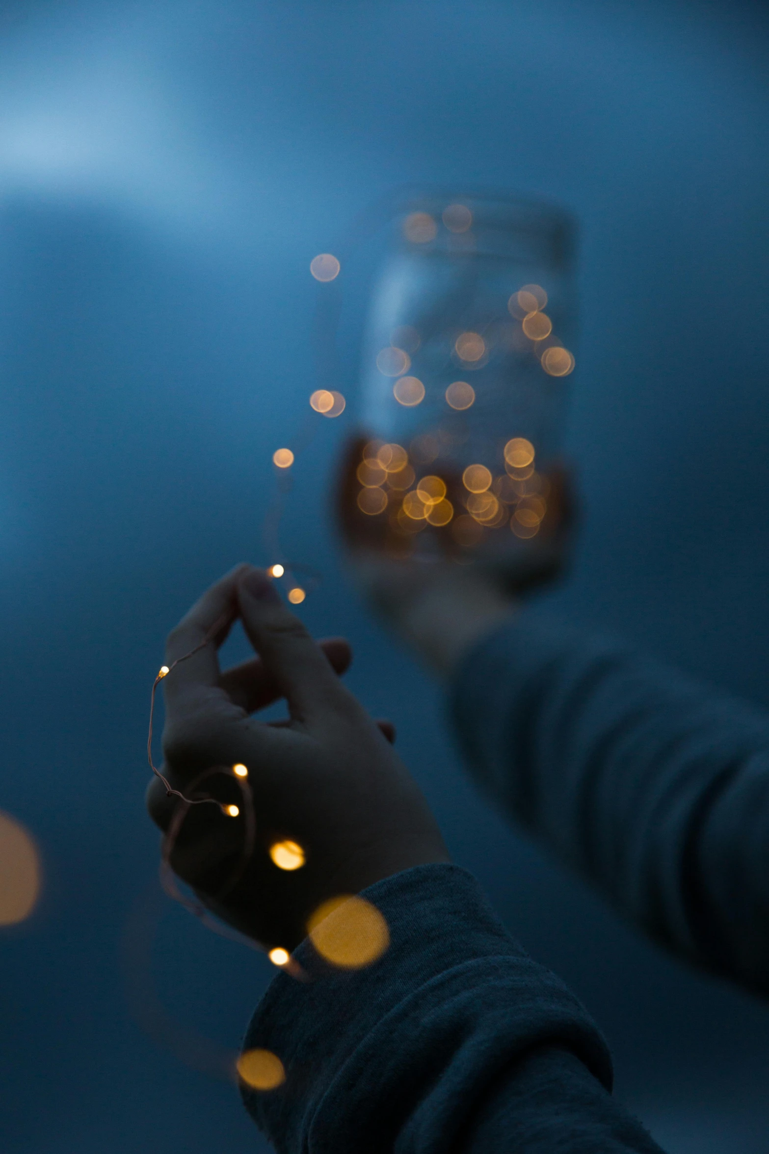 a person holding a glass of wine in their hand, a picture, pexels contest winner, conceptual art, floating lights, string lights, minimalist photo, dreamscape in a jar