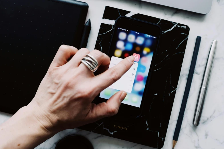 a close up of a person using a cell phone, by Julia Pishtar, trending on pexels, marble table, ipad pro, point finger with ring on it, 9 9 designs