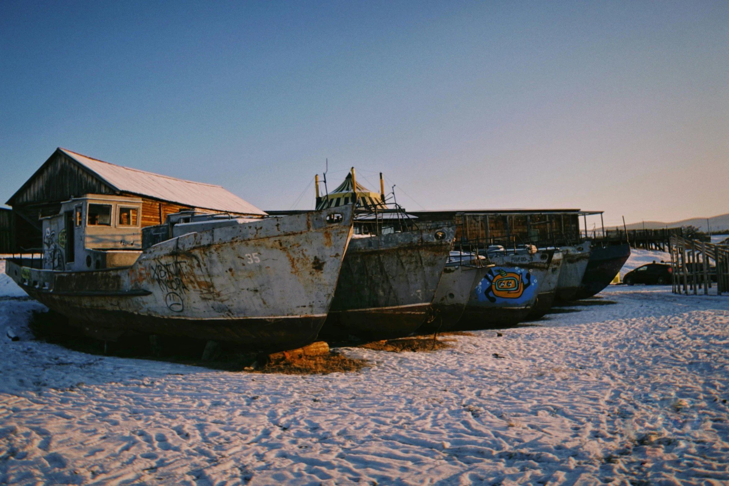 a couple of boats sitting on top of a snow covered field, a portrait, unsplash, land art, magical soviet town, museum photo, inuk, ground - level medium shot