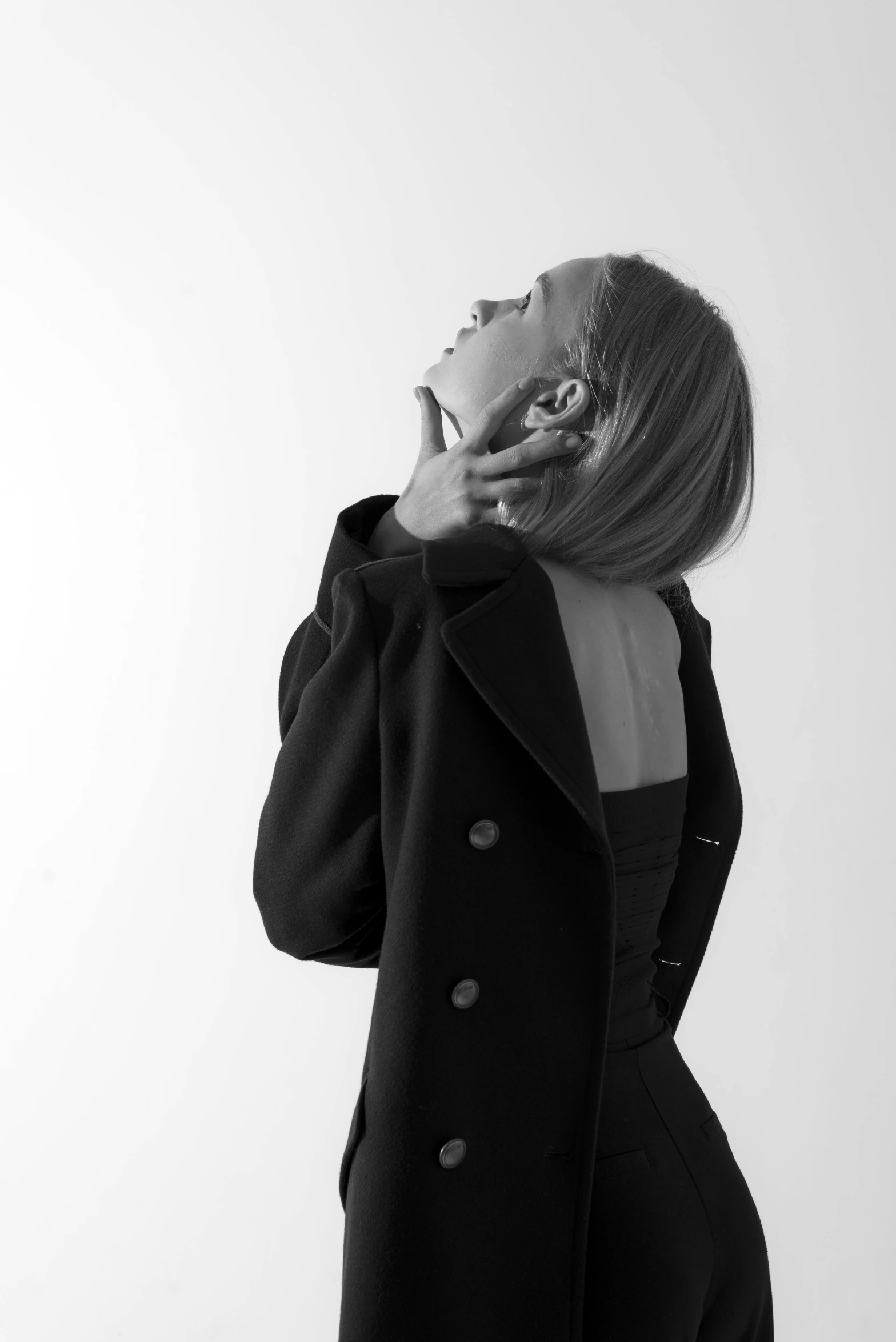 a black and white photo of a woman talking on a cell phone, a black and white photo, trending on pexels, minimalism, wearing black coat, doing an elegant pose over you, half turned around, a blond