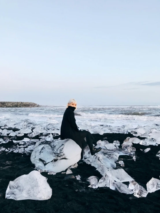 a man sitting on top of a pile of ice, by Julia Pishtar, trending on unsplash, black sand, ☁🌪🌙👩🏾, panoramic view of girl, plastic sea wrapped