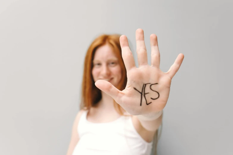 a woman holding up her hand with the word yes written on it, pexels contest winner, ( redhead, pregnancy, high forehead, kek