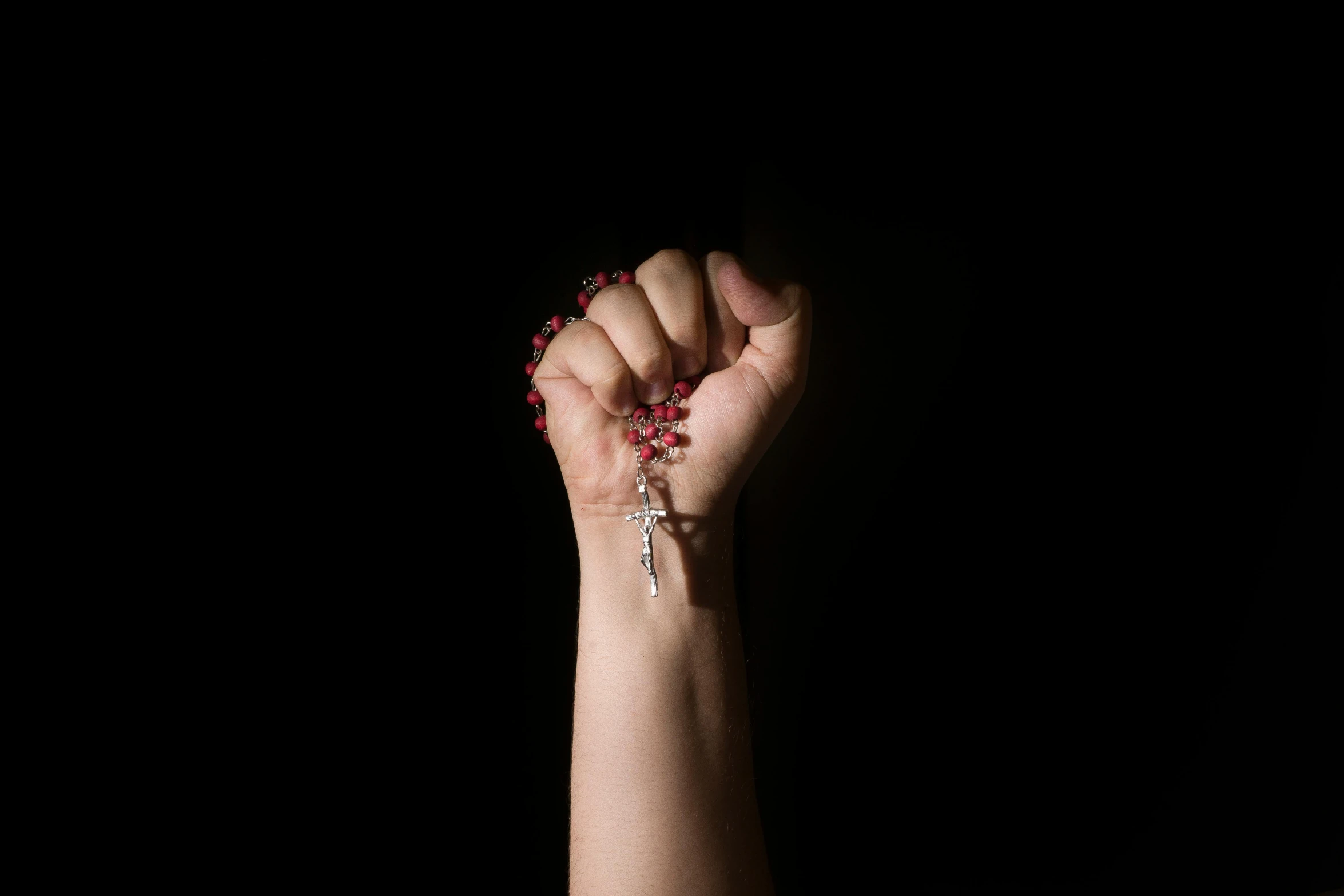 a woman's hand holding a rosary in the dark, an album cover, by Elsa Bleda, pexels contest winner, visual art, one fist raised high in triumph, red jewelry, marina abramovic, crucifix