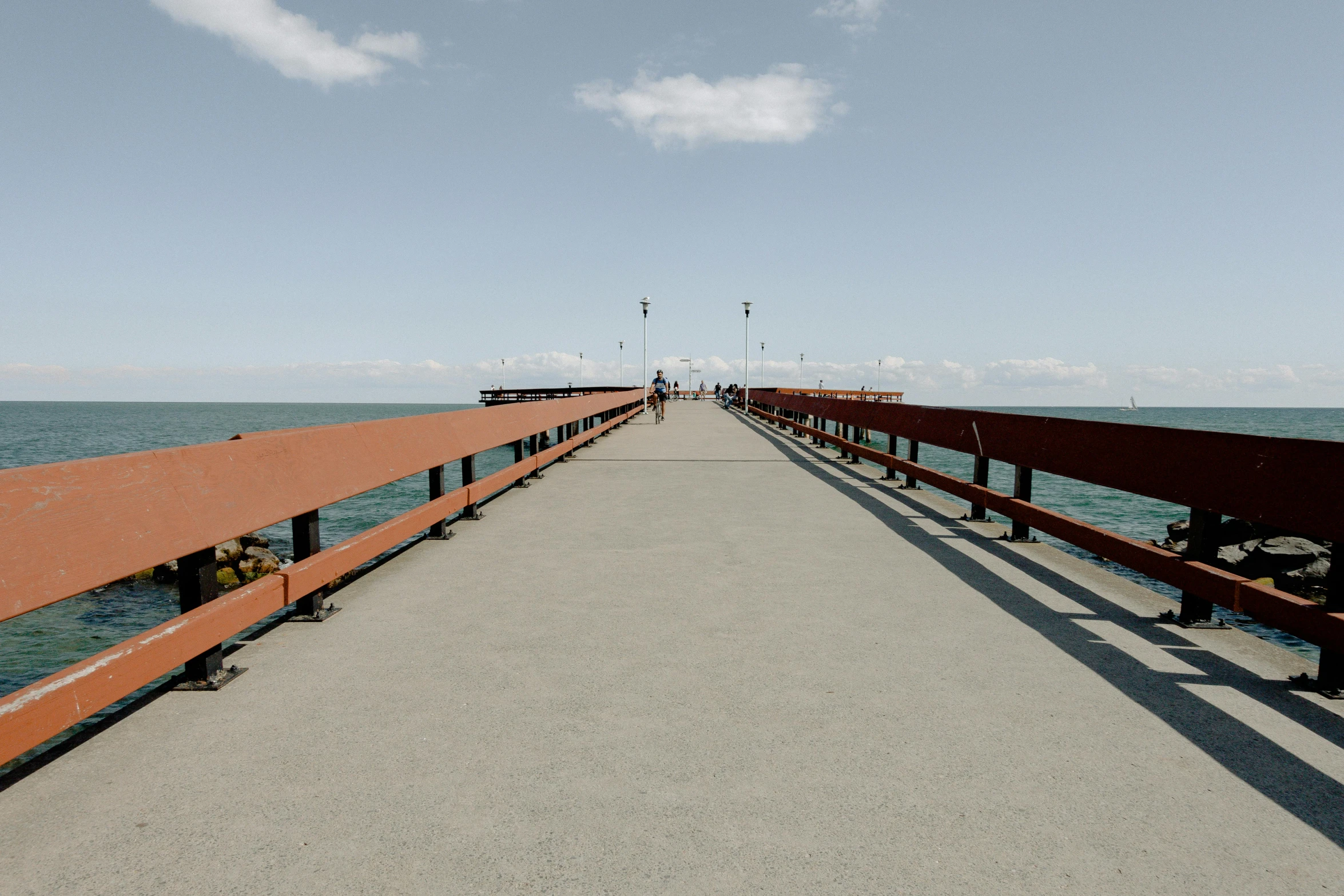 a long pier stretches out into the ocean, an album cover, by Niko Henrichon, unsplash, hurufiyya, bridge, brown, on a bright day, people walking around