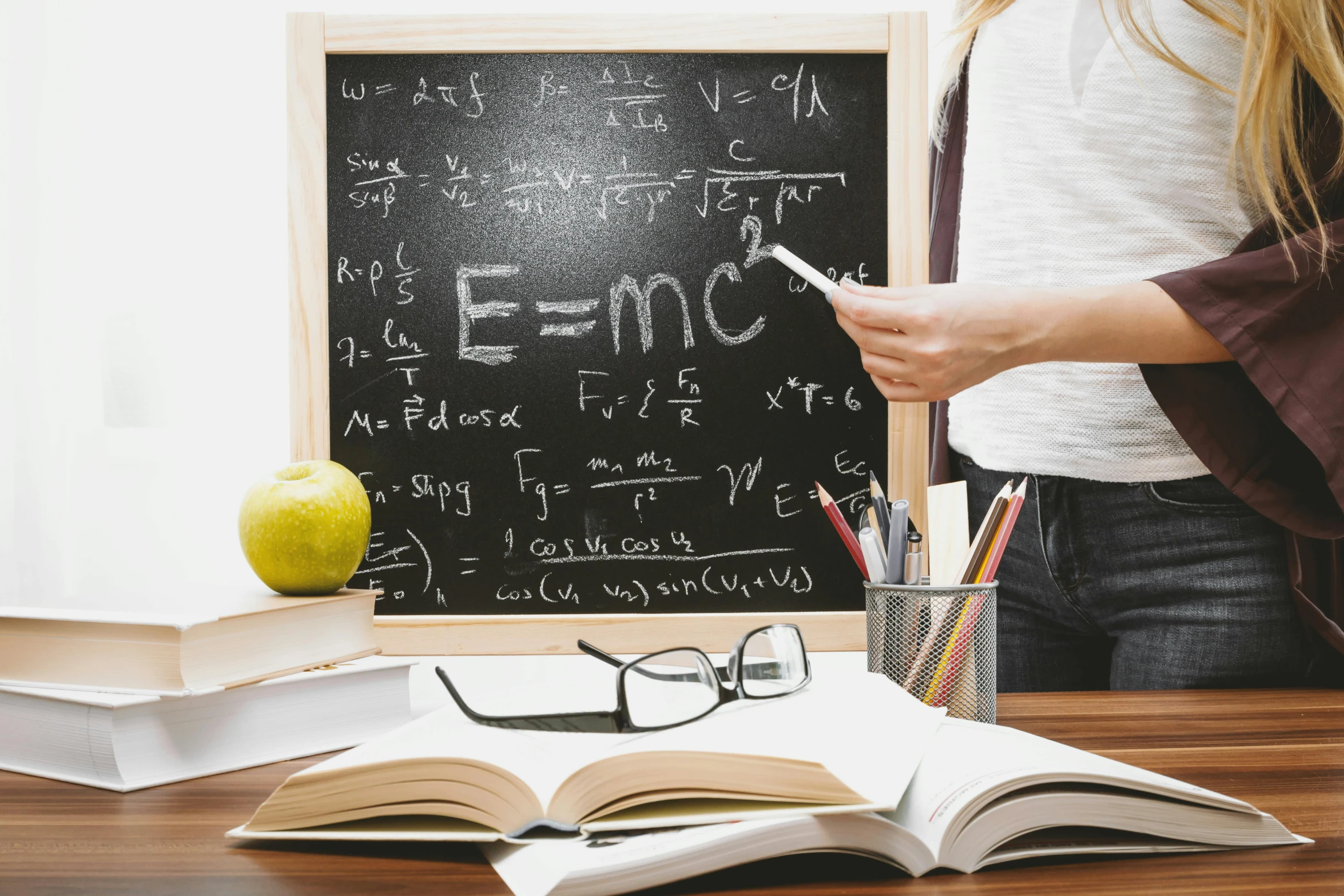 a woman standing in front of a blackboard holding a cell phone, a picture, by Meredith Dillman, pexels, academic art, wooden desks with books, equations, a person standing in front of a, inside an epic