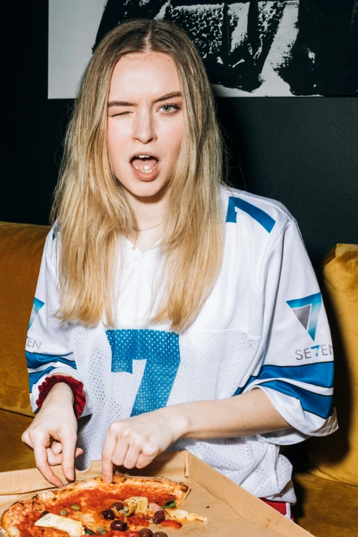 a woman sitting at a table with a pizza in front of her, an album cover, inspired by Louisa Matthíasdóttir, featured on reddit, holding a football, with index finger, portrait of kim petras, on a couch