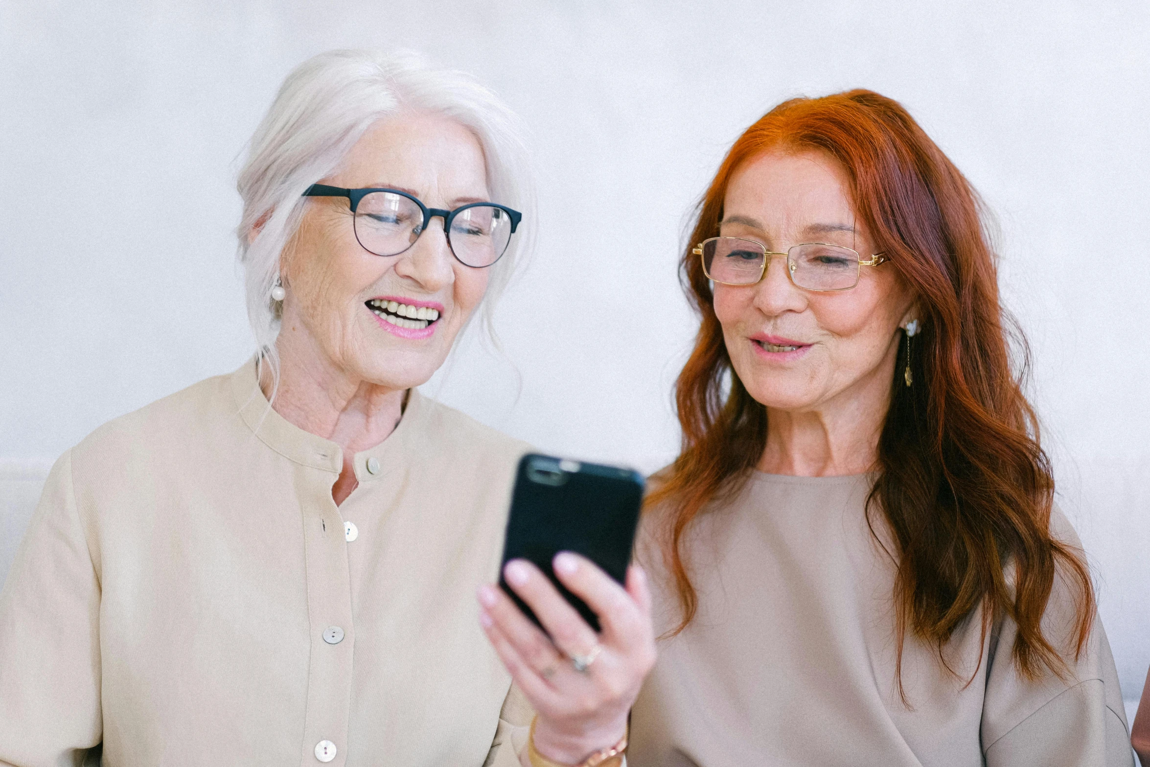 two women sitting on a couch looking at a cell phone, a photo, trending on pexels, renaissance, an old lady with red skin, with square glasses, avatar image, silver haired