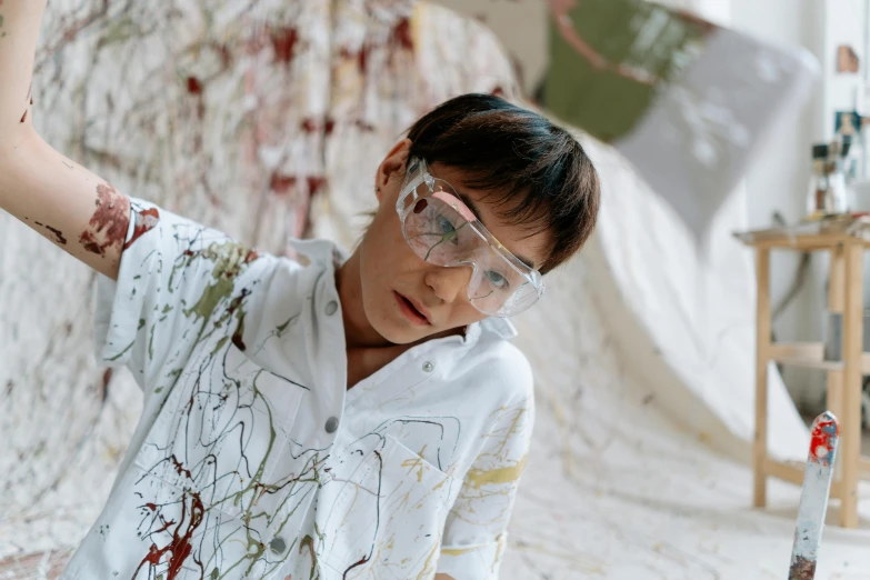 a boy in a white shirt and goggles holding a paintbrush, inspired by Shōzō Shimamoto, trending on pexels, action painting, margiela campaign, wearing lab coat and a blouse, mina petrovic, baselitz