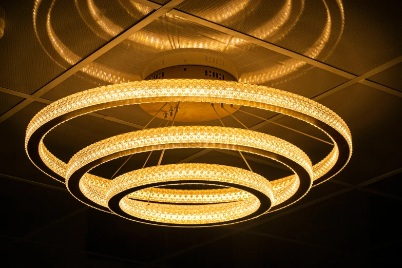 a large circular chandelier hanging from the ceiling, by Adam Marczyński, golden lighting, technological rings, gallery lighting, sparkly