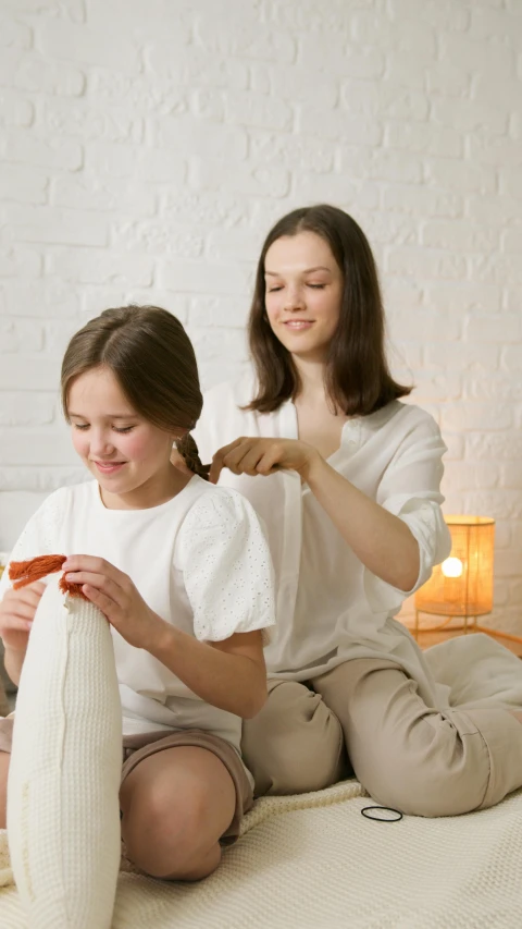 a couple of women sitting on top of a bed, on a white table, kids playing, himalayan rocksalt lamp, long braided hair pulled back