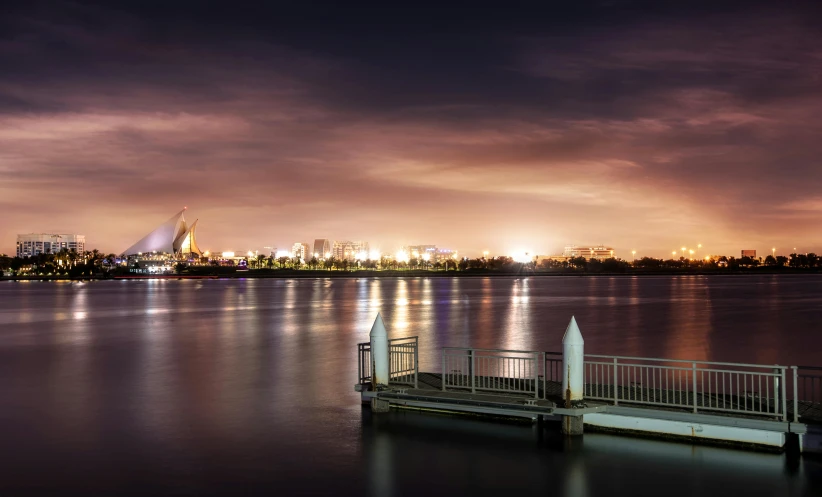 a dock next to a body of water with a city in the background, inspired by Edwin Deakin, pexels contest winner, hurufiyya, arabian night, iso 1 0 0 wide view, photo taken with canon 5d, soft glow