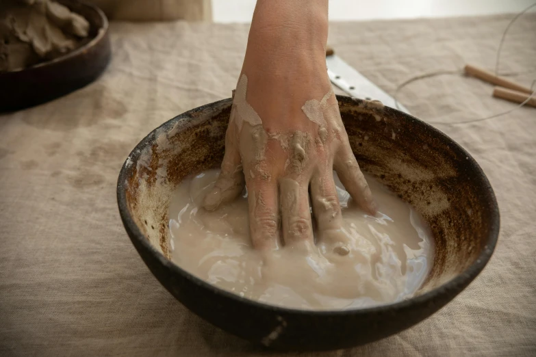 a close up of a person's hands in a bowl of mud, inspired by Sarah Lucas, process art, organic ceramic white, 8l, pouring, delightful surroundings